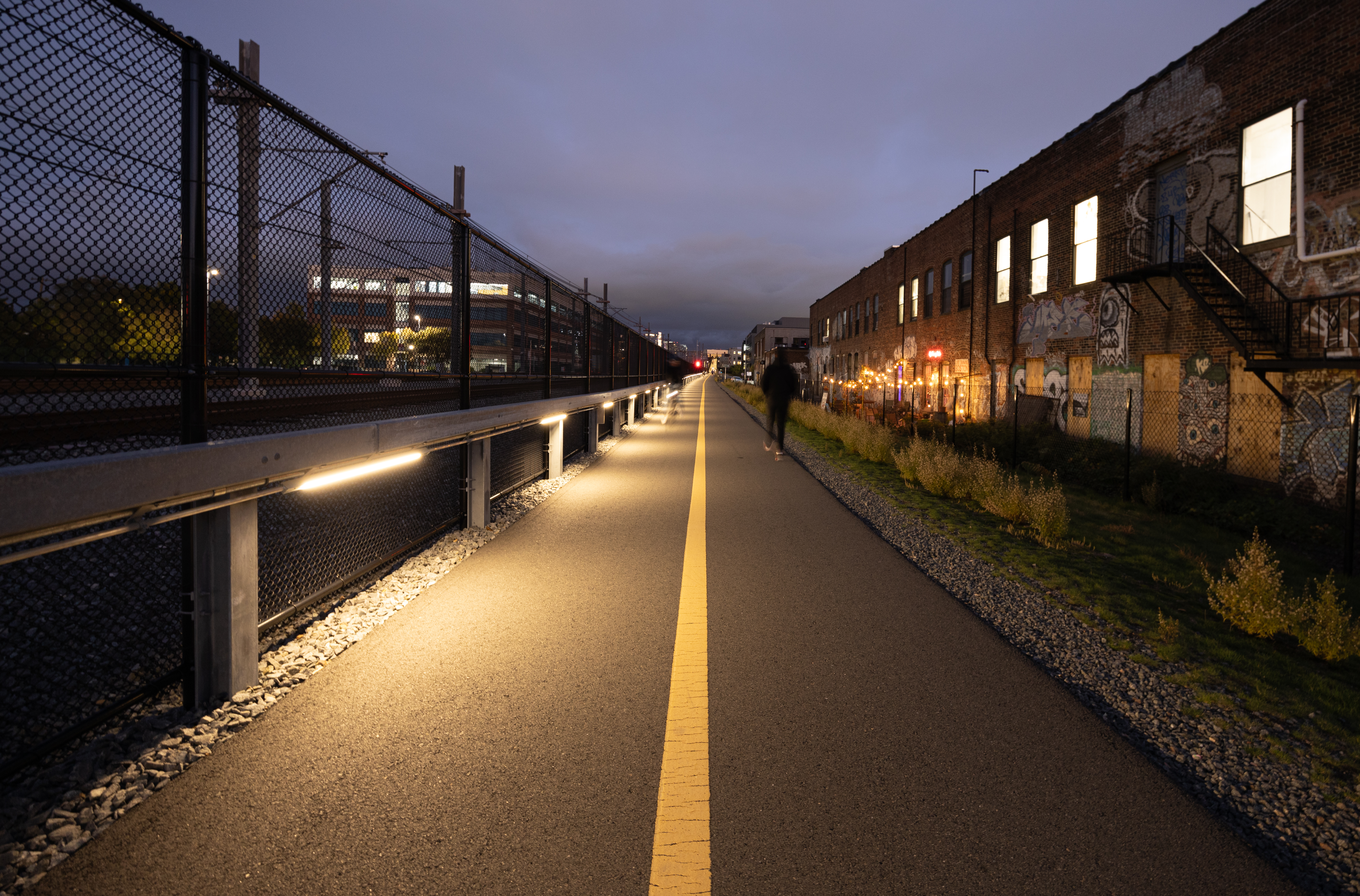 A view of the community path facing eastward with new lighting along the railing shedding light on the path. 