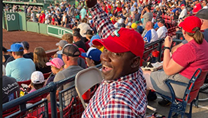 Man in wheelchair in stadium bleachers smiling at Red Sox Game on Disability Pride Game Night outing