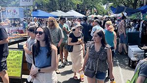 Dozens of Somerville residents walk together through an arts festival under a bright blue sky. 