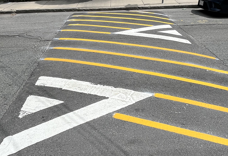 Fresh yellow and white road markings highlight a speed hump on a residential street in front of houses and parked cars.