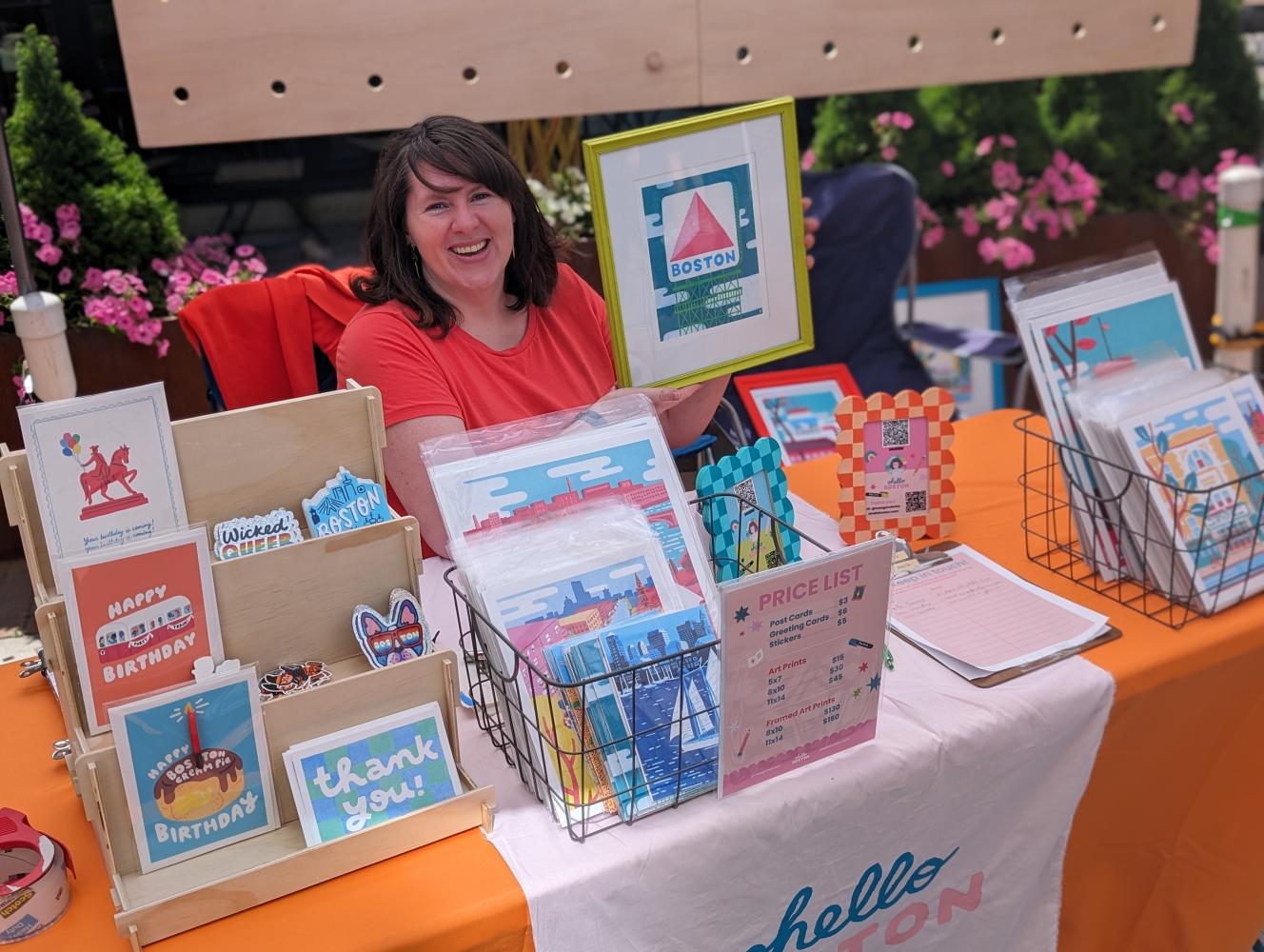 A woman at a table with art on display. 