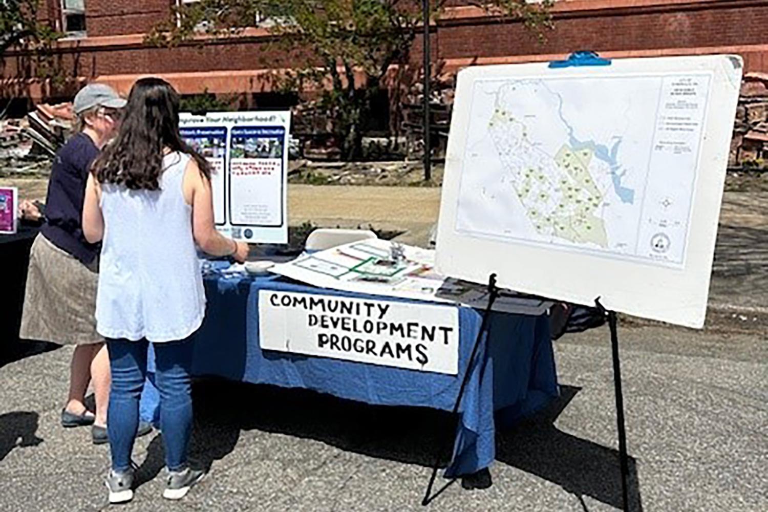 A woman standing at at table displaying community development programs information. 