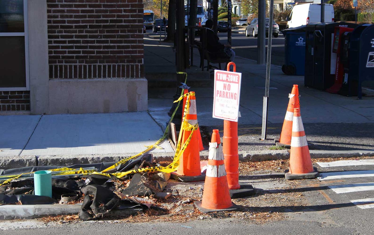 Construction cones and a no parking sign next to a pothole being repaired.