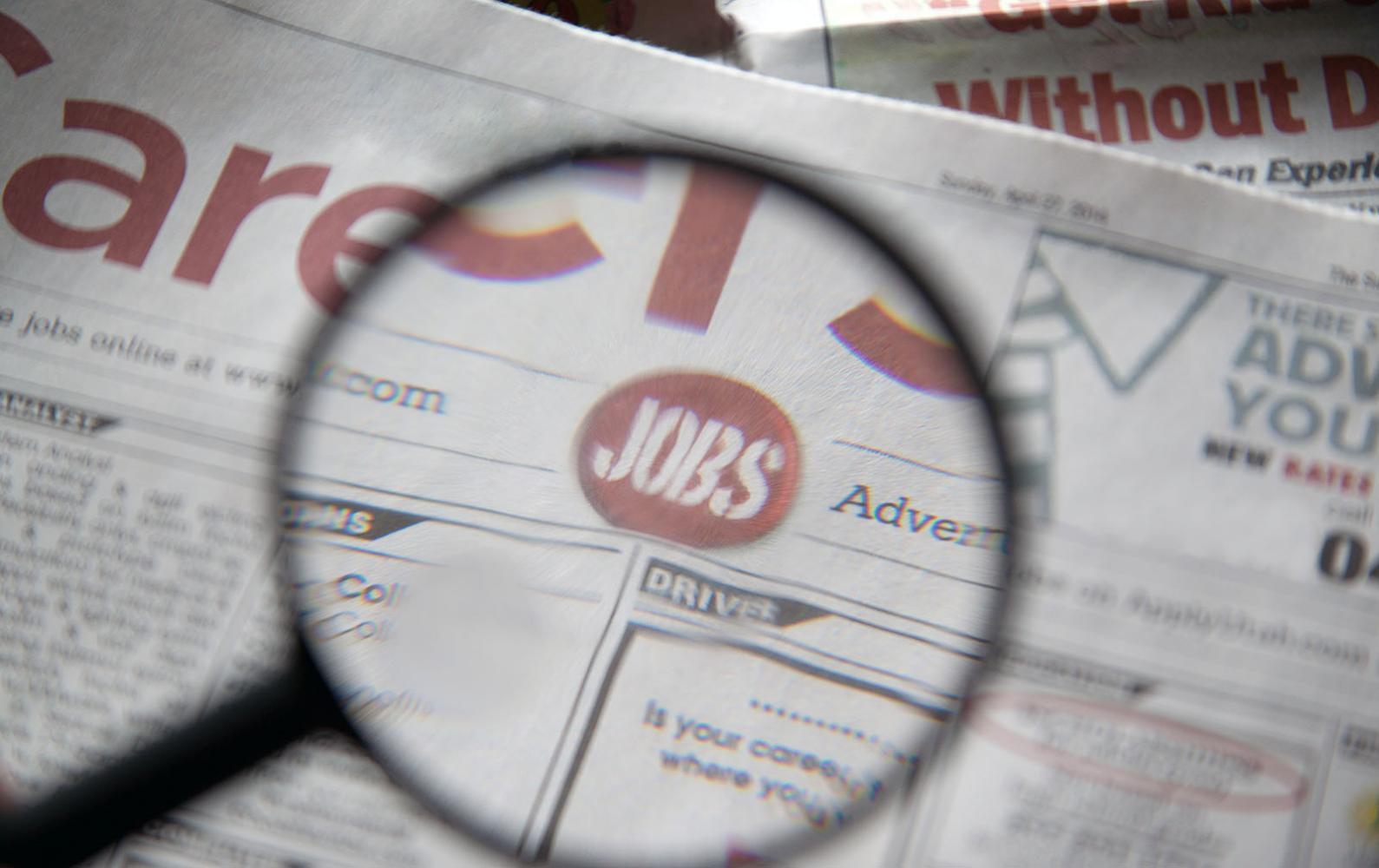 Magnifying glass reveals the word "jobs" on the page of a newspaper