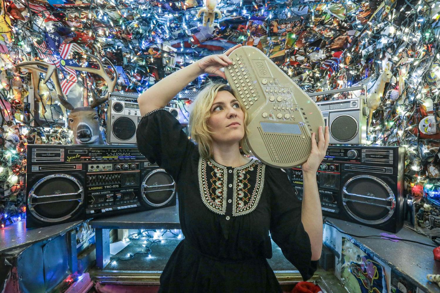 Photo of Arts Council director Lydia Warren in a black shirt surrounded by musical instruments and artwork. 