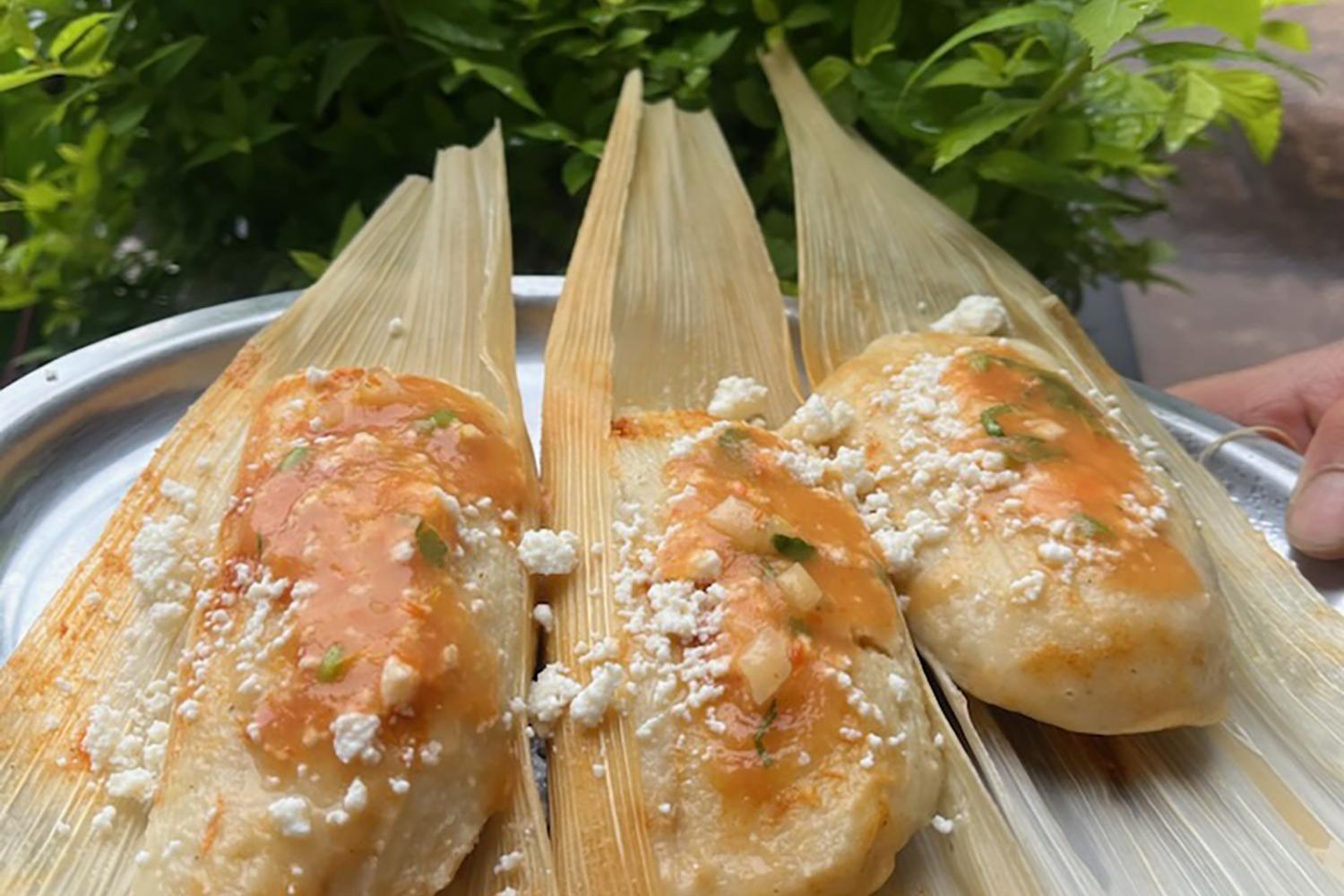 Three chicken chuchitos on corn husks, topped with red sauce and crumbled white cheese.