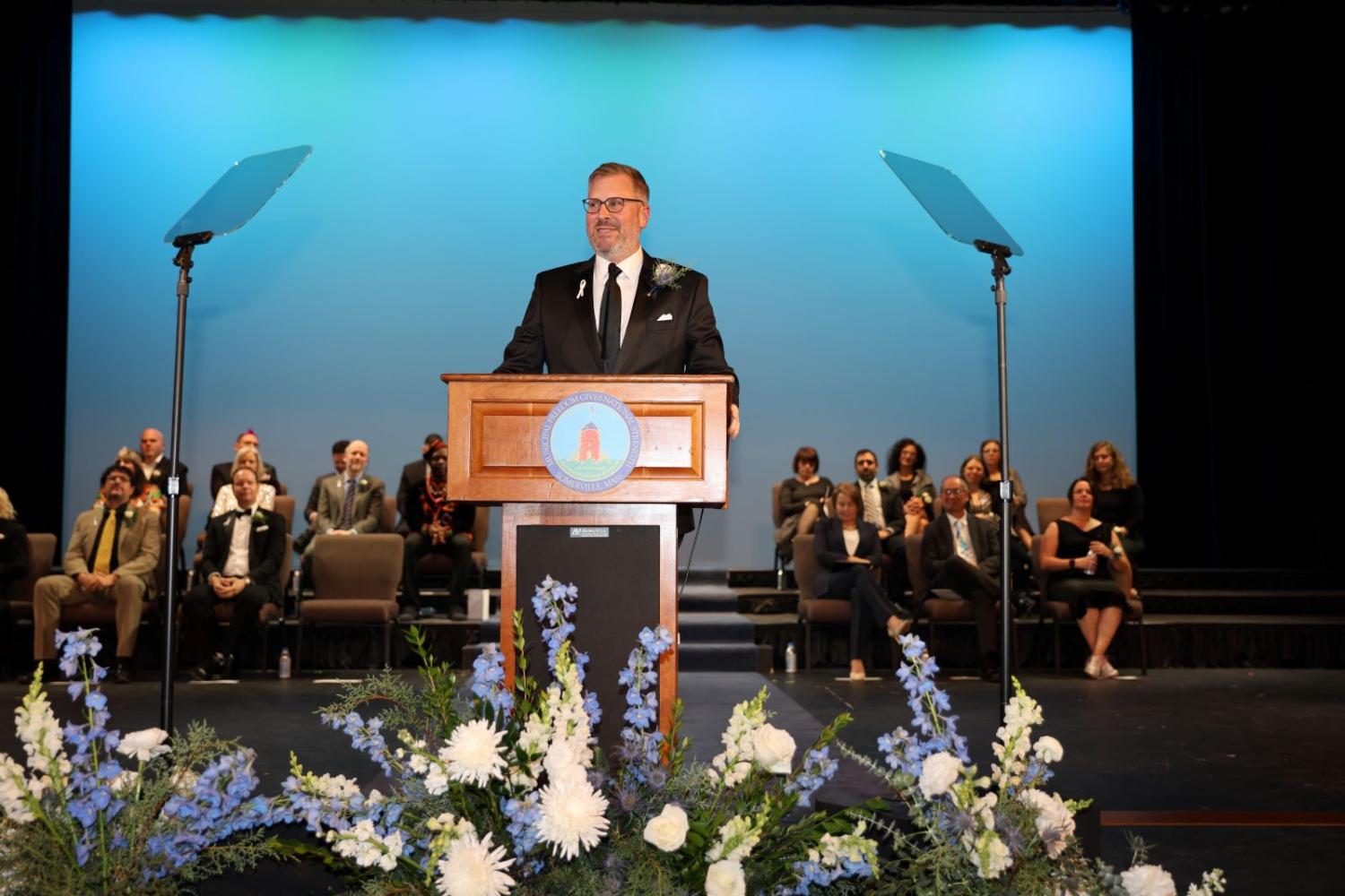 Mayor Jake Wilson delivers his inaugural address on stage in front of a blue background. 