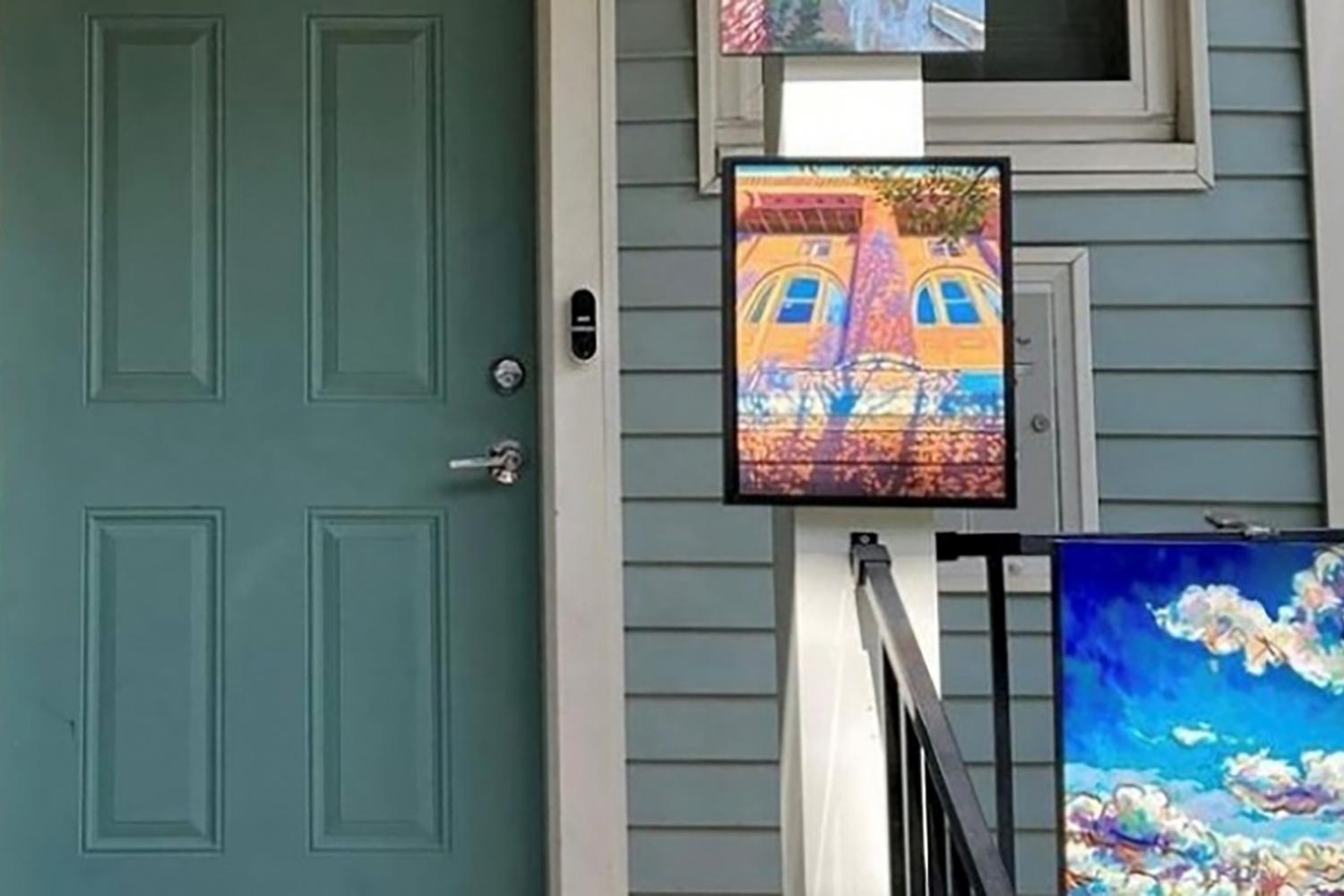 Colorful paintings displayed on the front porch of a house for an outdoor art sale.