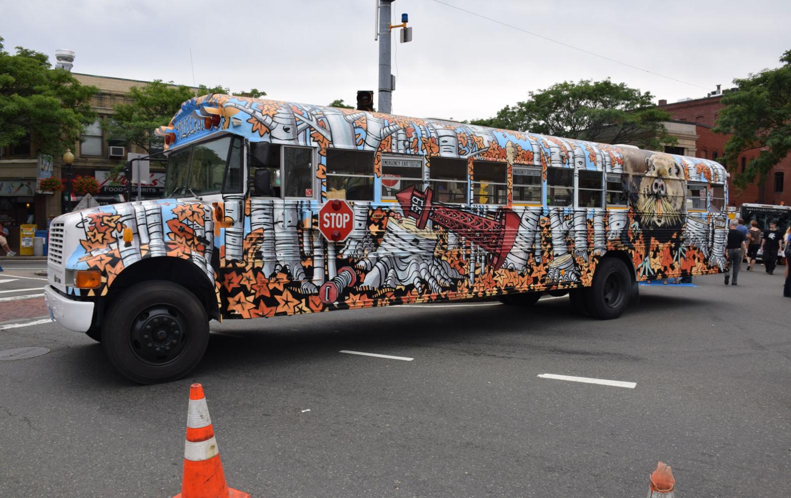 A painted schoolbus at the 2014 Artbeat festival features trees, animals, and a lighthouse.