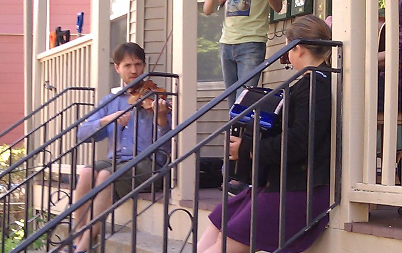 Two City residents play an accordion and a fiddle on a porch during PorchFest 2012