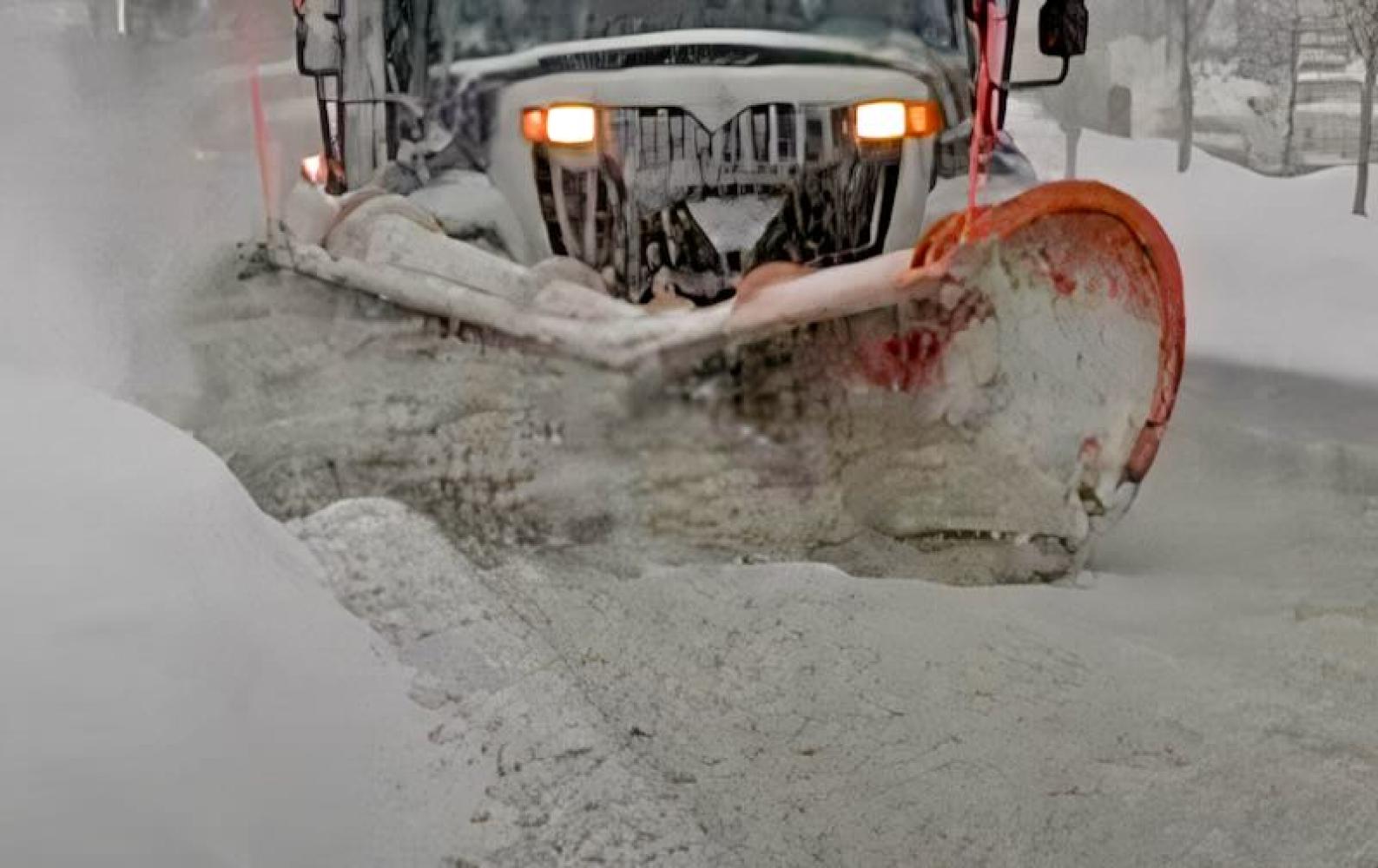 Front-facing snow plow pushing through deep snow on a city street. 
