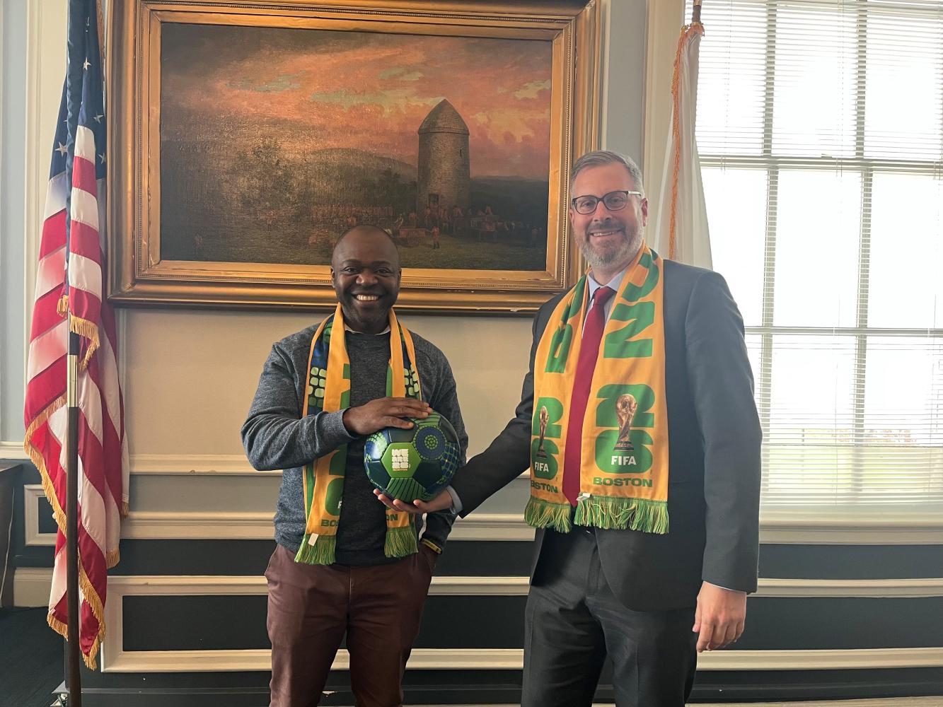 Councilor At Large Will Mbah and Mayor Wilson wearing world cup scarves and holding soccer ball in Mayor's Office