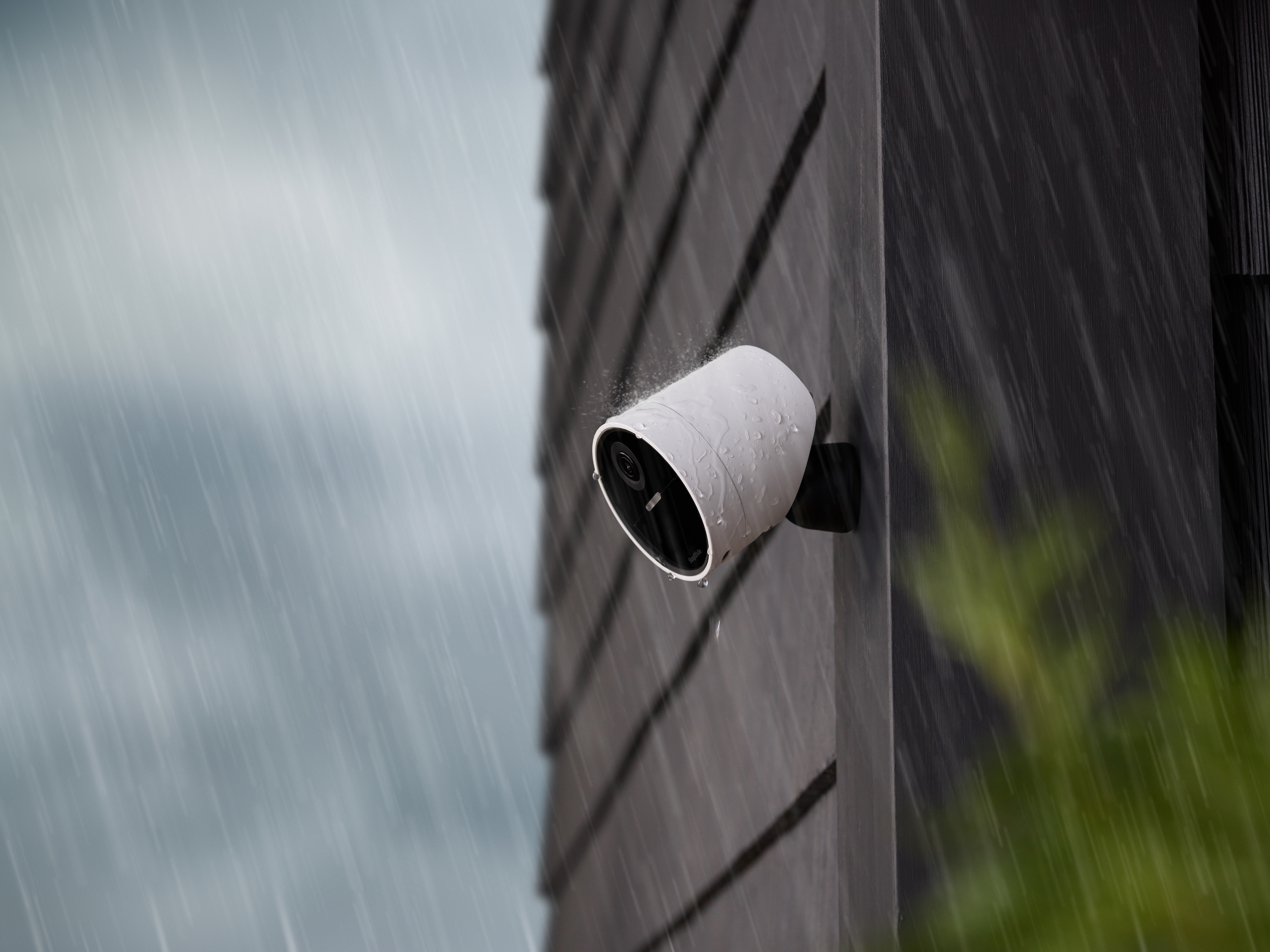 An Outdoor Camera affixed to the side of a building, with rain coming down.