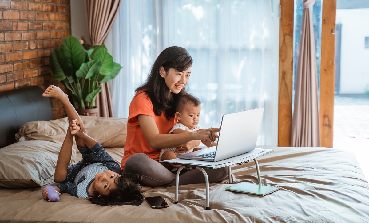 Mother working from home  on laptop with two young children.
