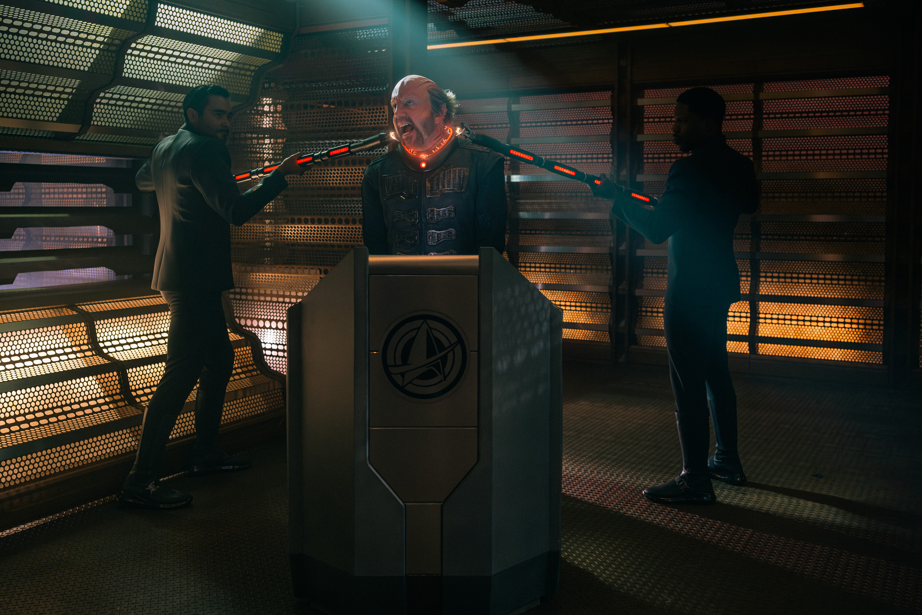 An alien man is restrained by two other alien men