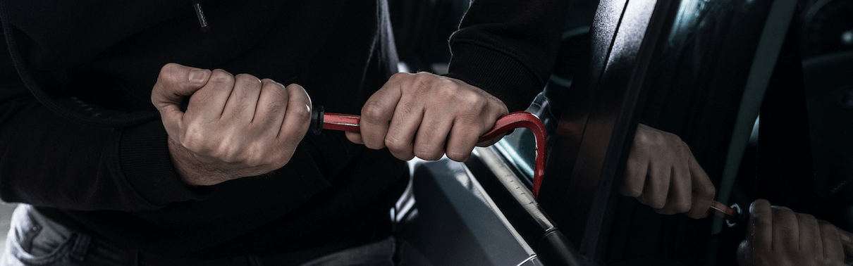 Thief trying to gain access to a vehicle using a small crowbar on the window