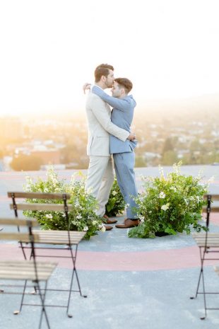 Photo of a same sex couple hugging surrounded by flowers on the helipad
