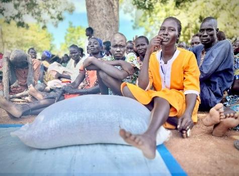 A group of people sitting on the ground. A bag of food in the foreground.