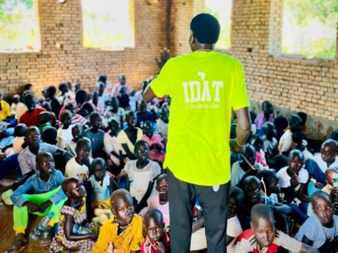 A person in a yellow shirt speaking to a group of people