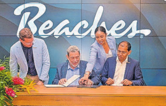 Prime Minister Dr Ralph Gonsalves, centre, about to sign an agreement with the chief executive officer of Sandals Resorts International, Adam Stewart, standing, on Monday. CMC PHOTOS