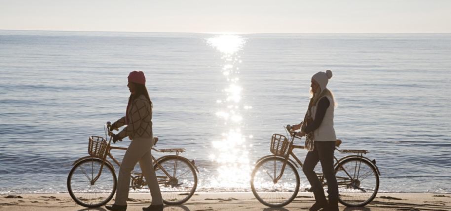 2 womens walking with their bicycle near the beach