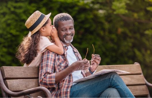 Young child whispering in mans ear on a bench outside