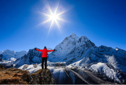 hiker on a peak with their arms spread looking at a higher peak