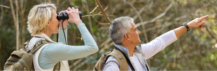 Woman with binoculars and man pointing in woods on a hike