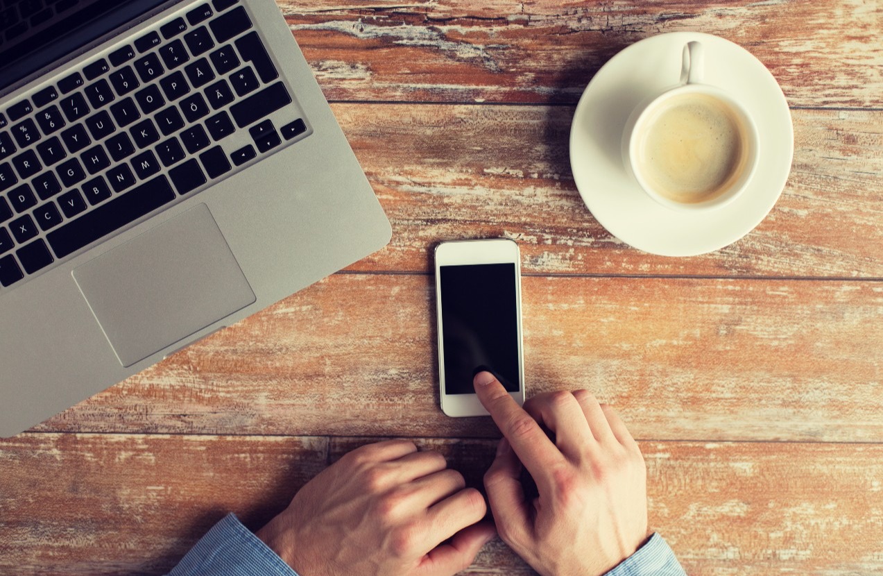 Man checking his iPhone with coffee and laptop