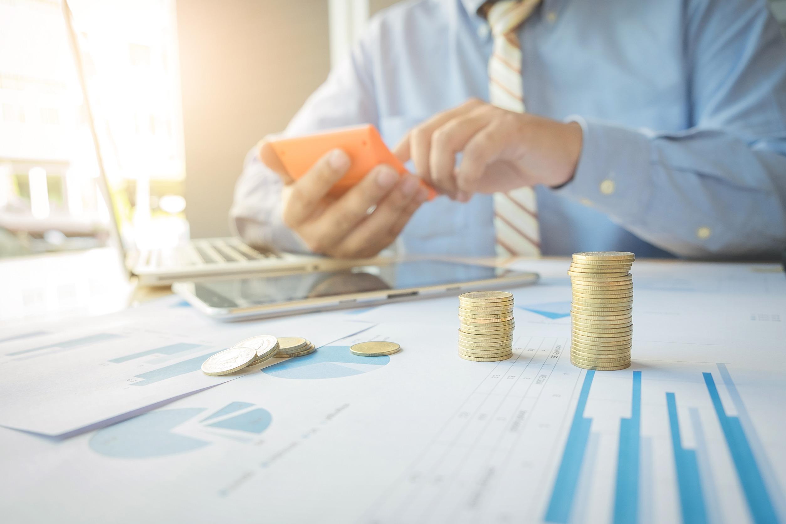 man in front of laptop with stacks of coins and printed charts