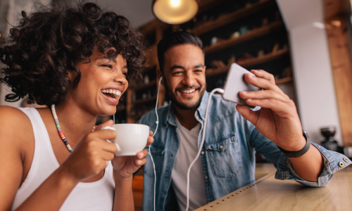 two people at a coffee shop drinking coffee and looking at a cellphone, smiling