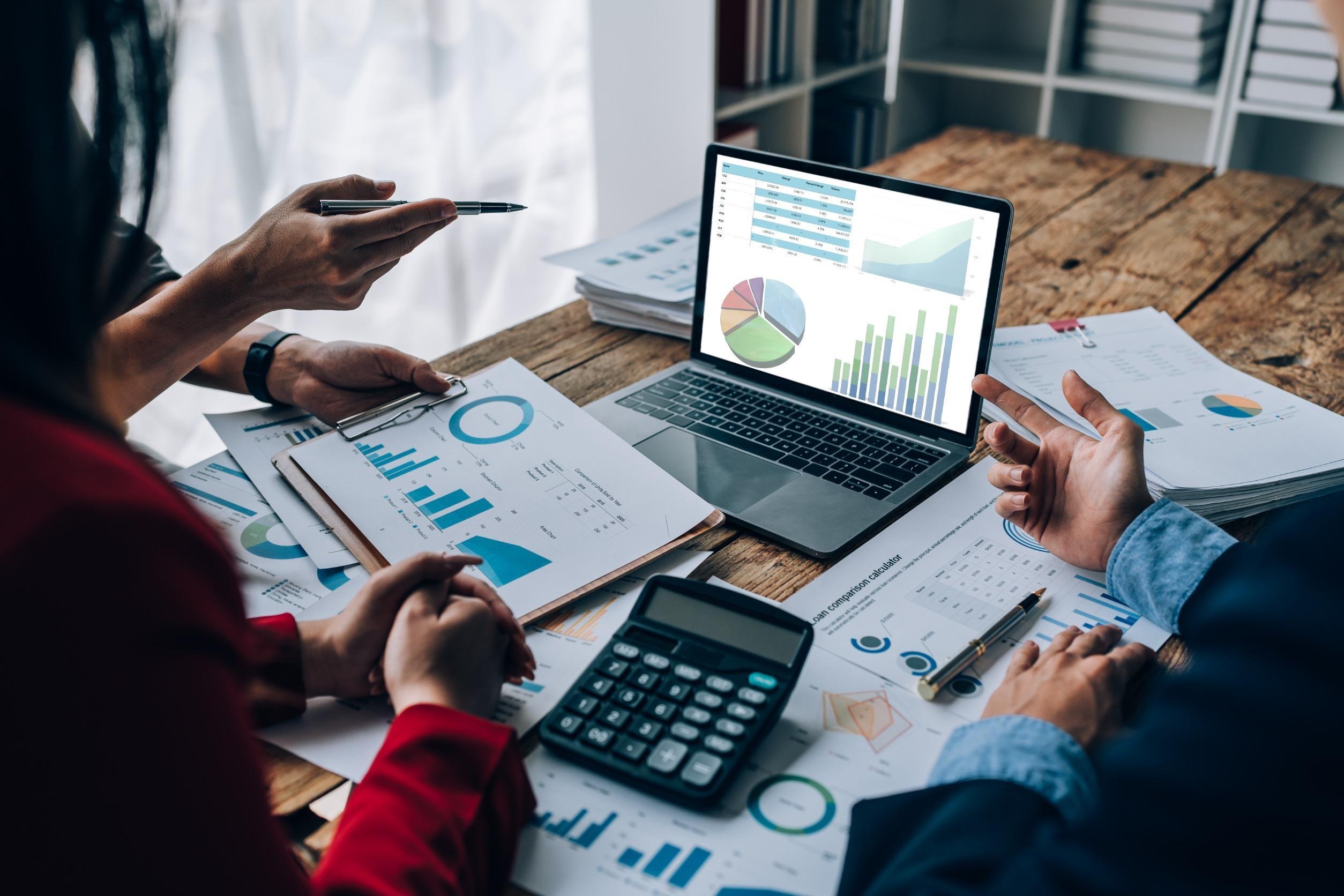 three people around a laptop with several charts printed out in front of them