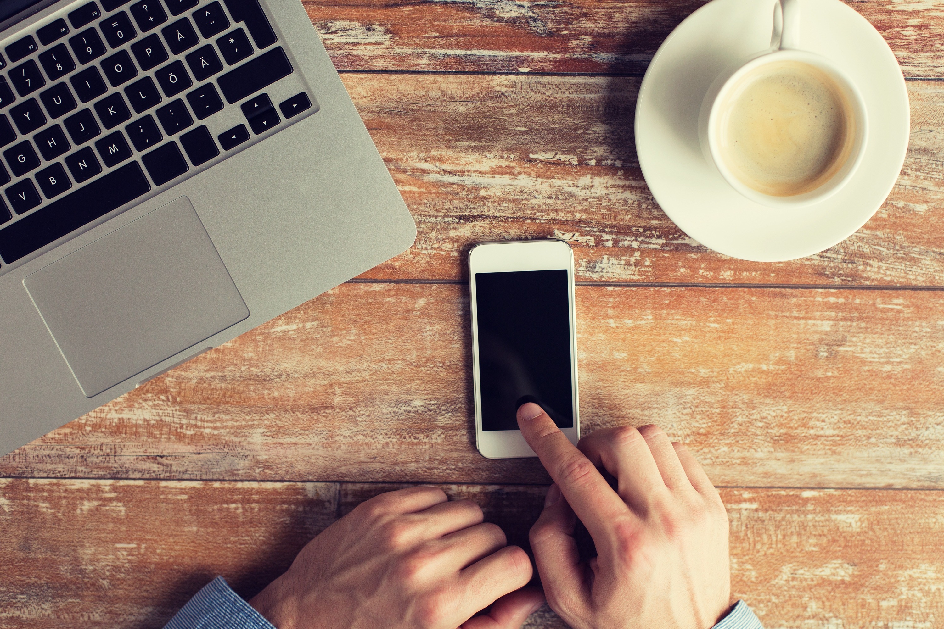 Man checking his iPhone with coffee and laptop