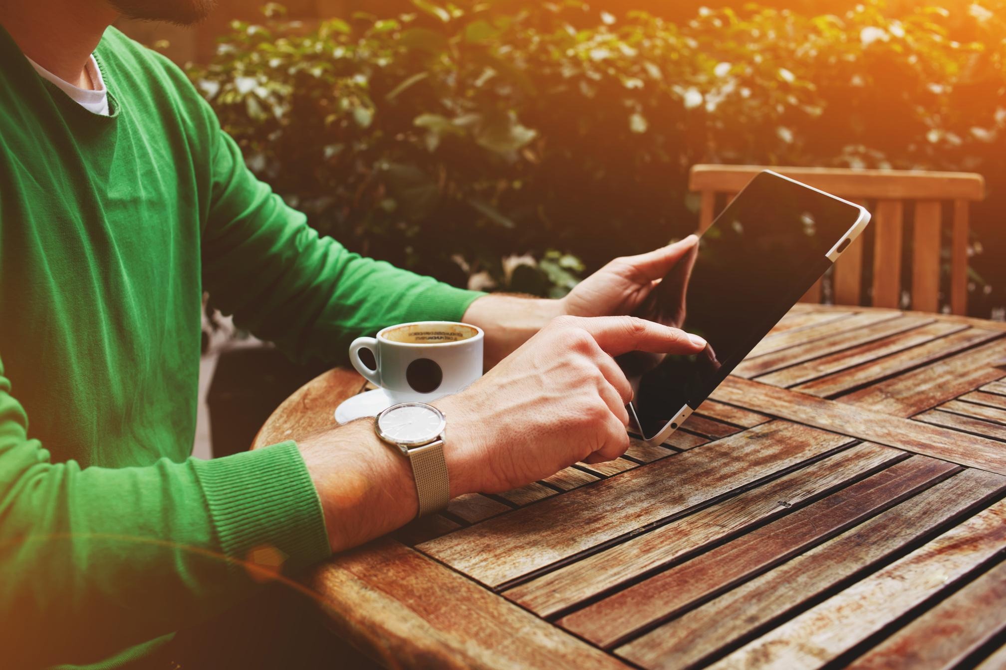 Man holding a tablet with a cup of coffee