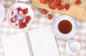 an open journal, a cup of tea and strawberries dipped in cream on a table