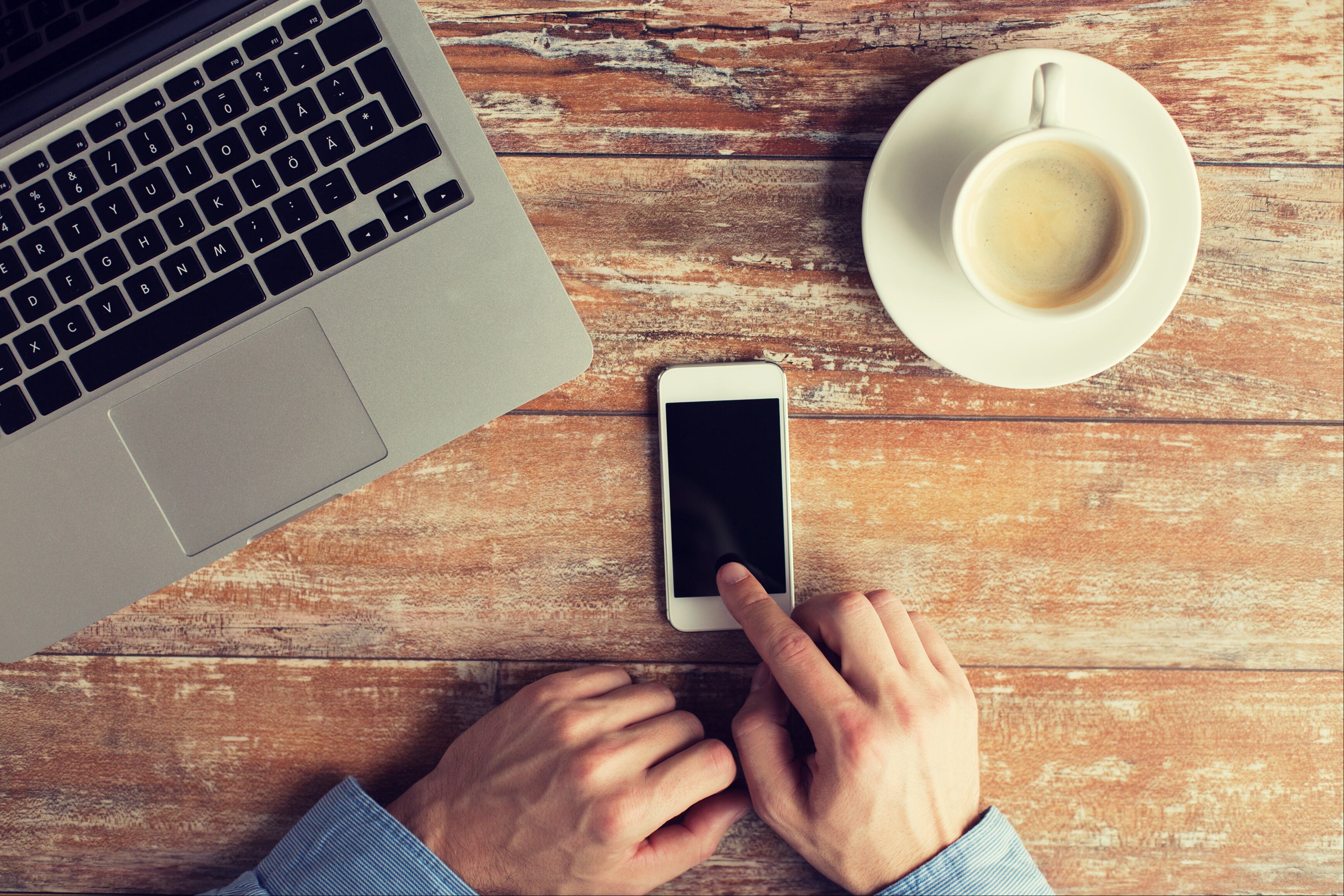 Man checking his iPhone with coffee and laptop