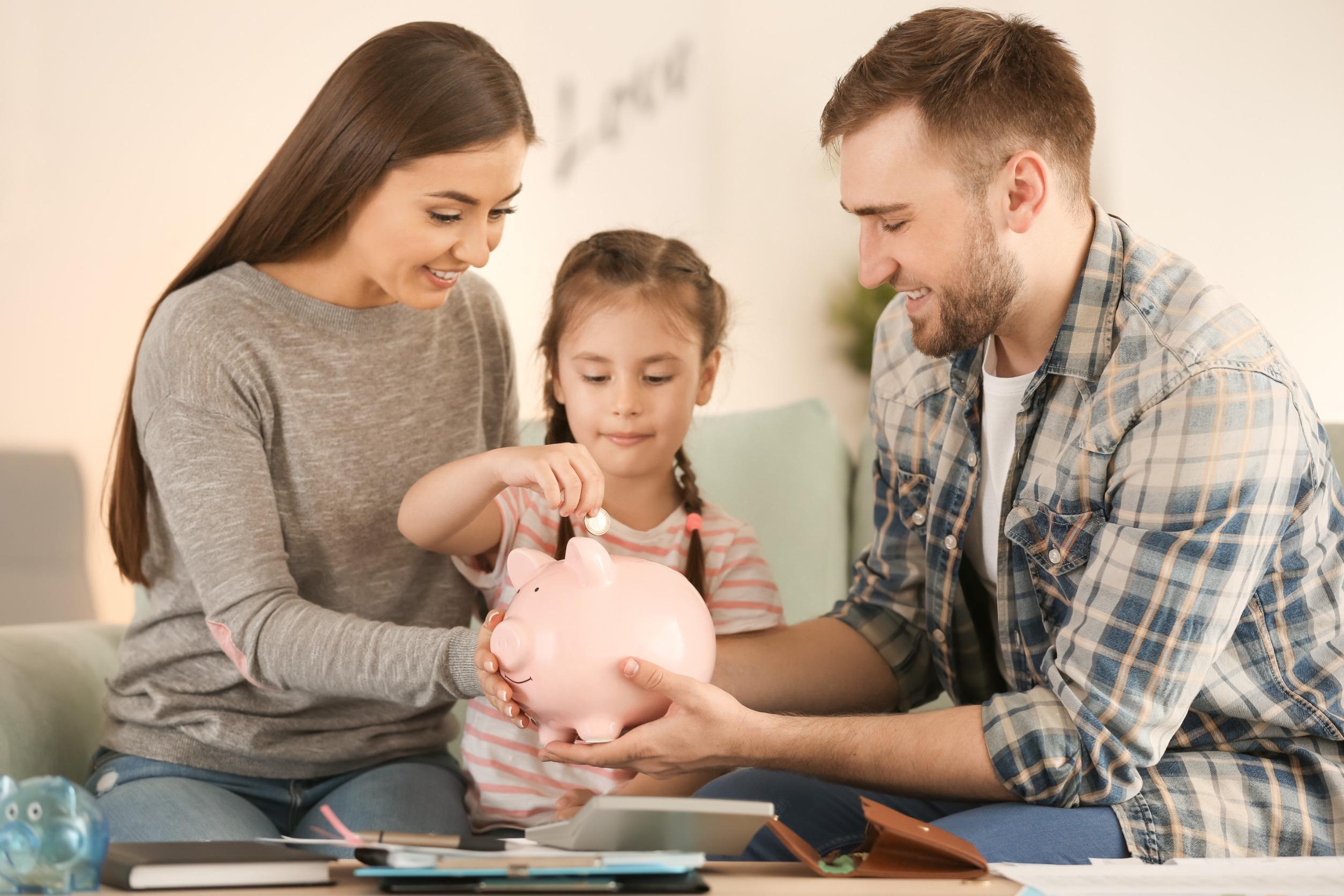 parents teaching their child how to save with a piggy bank
