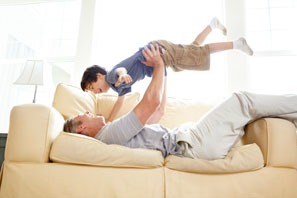 grandfather lifting his grandson above him like an airplane on a couch and both smiling