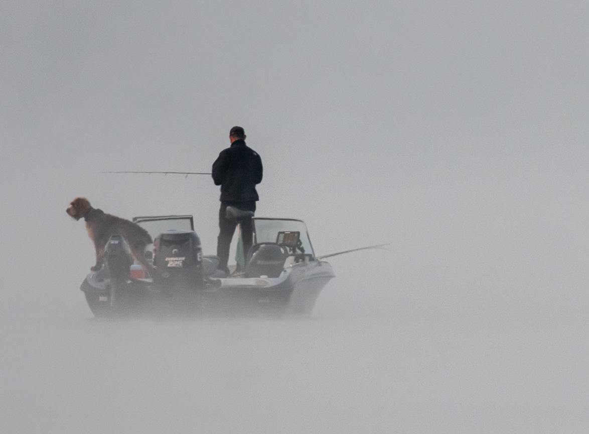 Photo of a man on a boat with a dog while fishing