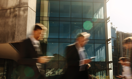two businessmen looking at their cellphone outside next to a modern building