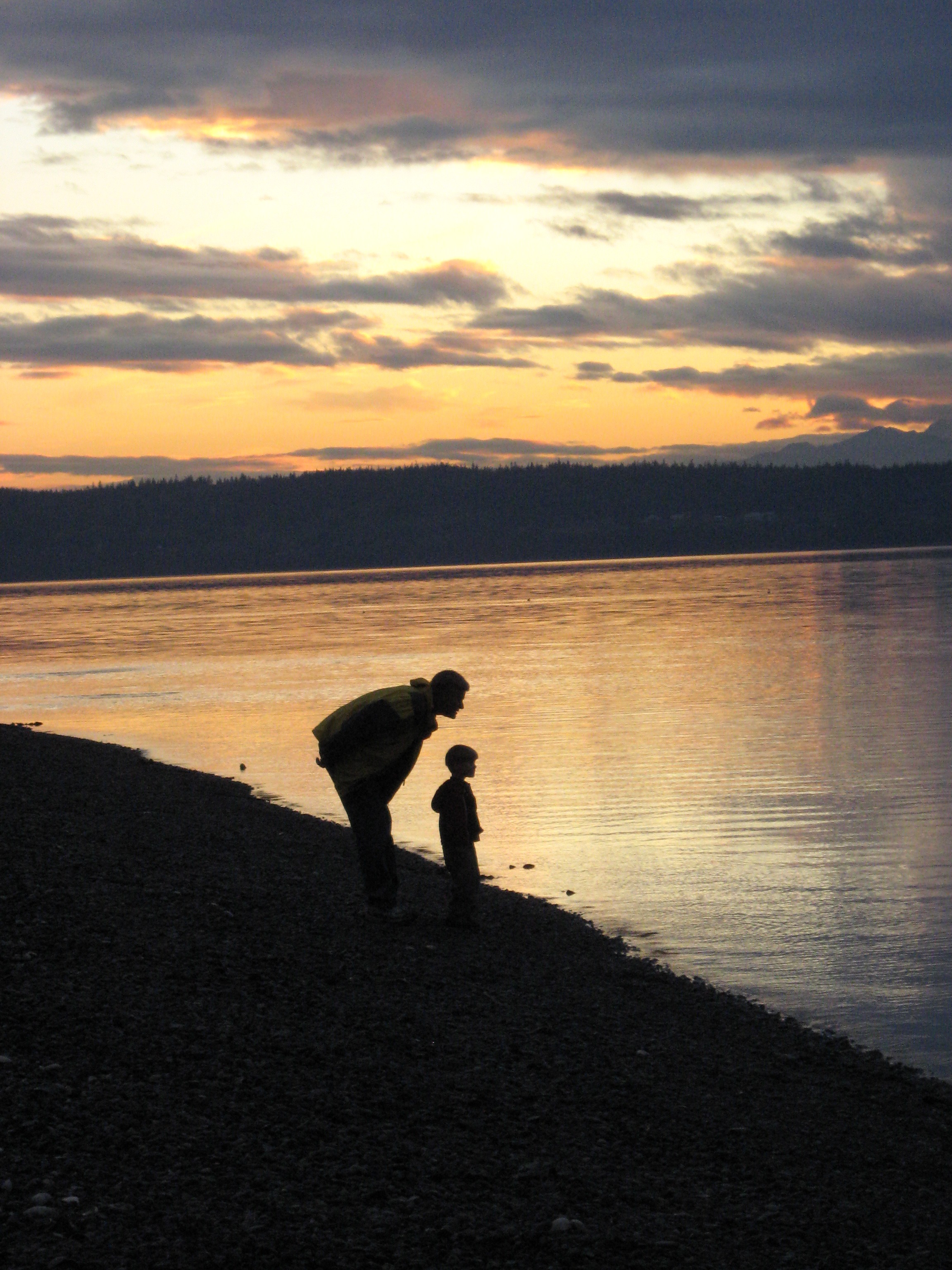 Adult and child standing next to a lake as the sun is setting.