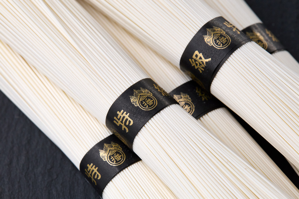 明治時代から守り続けられてきた日本屈指の素麺。中でも黒帯の「ひね特級」は、かかる手間も時間もスペシャル｜帰省の手土産、暑中お見舞いに、夏の贈り物に。1年熟成のコシと舌触り「揖保乃糸 ひね特級」｜揖保乃糸（ミニ木箱入り）
