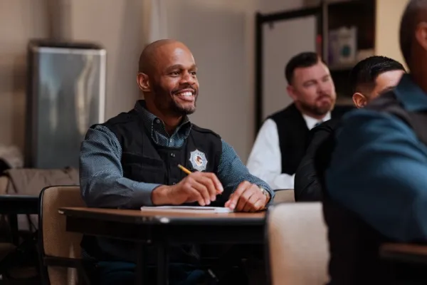 black male educational officer at desk in a class of other people