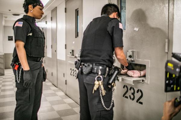 Officers putting cuffs on an incarcerated person in a cell through the door hatch