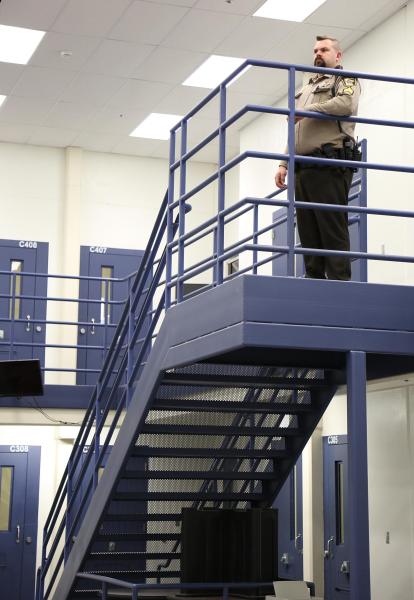 a male officer stands a the top of a set of stairs in a pod overlooking the unit