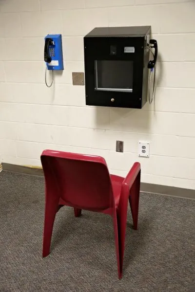 A chair in front of a video visitation station attached to a white cinderblock wall