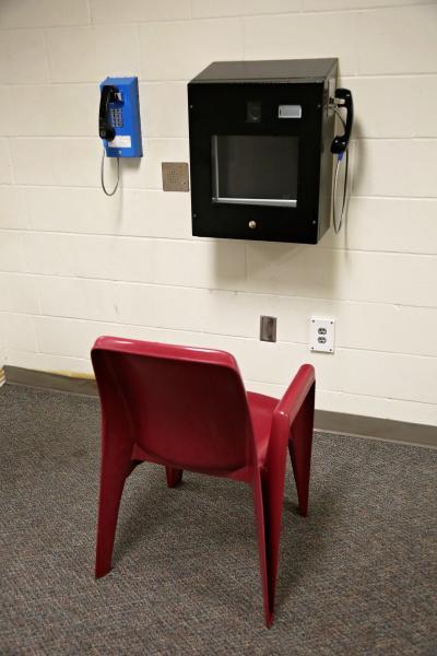 A chair in front of a video visitation station attached to a white cinderblock wall