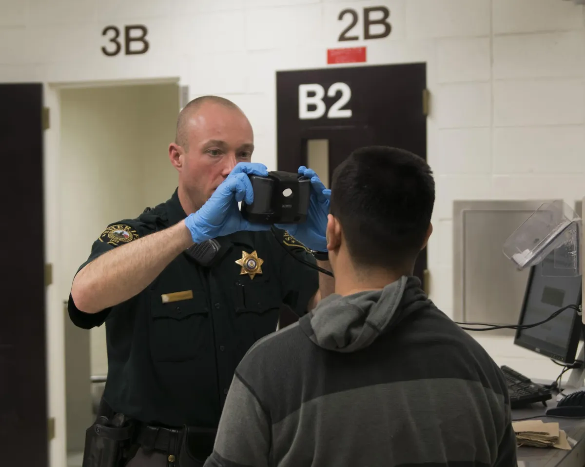 A correctional officer takes a photo of a man during the intake process