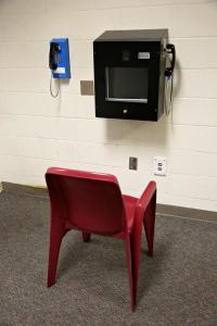 A chair in front of a video visitation station attached to a white cinderblock wall