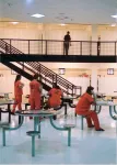 several inmates sit at tables in their pod while a corrections officer walks the second floor